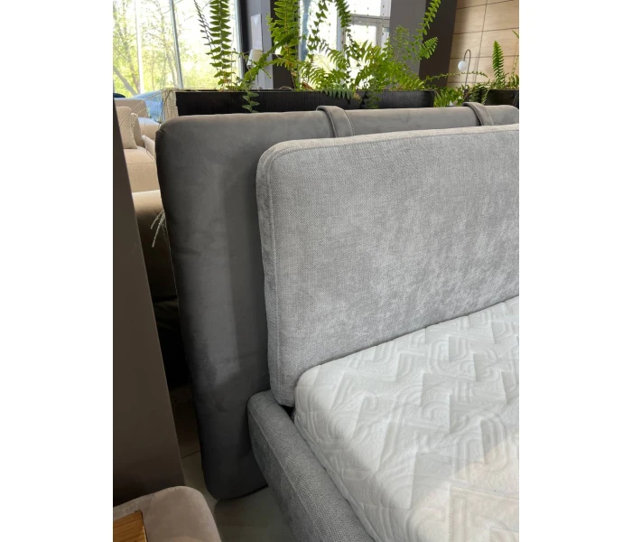 Сіре ліжко на високих металевих ніжках з подвійним м’яким узголів’ям-подушками